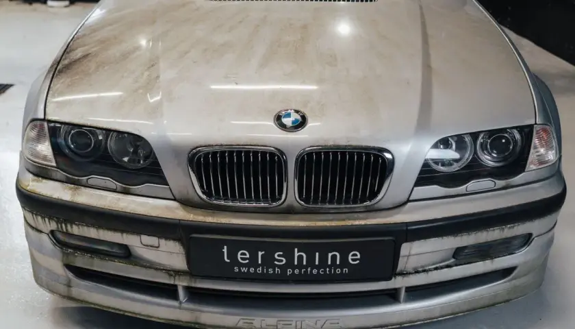 En smutsig silverfärgad BMW med synliga fläckar på huven och stötfångaren. Dags att avfetta bilen för att få fram dess glans.