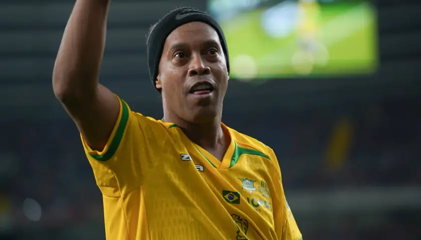 Ronaldinho w żółtej koszulce z zielonymi akcentami, podnosi rękę.