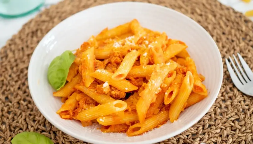Un plato de macarrones con atún, cubiertos con salsa de tomate y queso rallado, adornado con hojas de albahaca fresca.