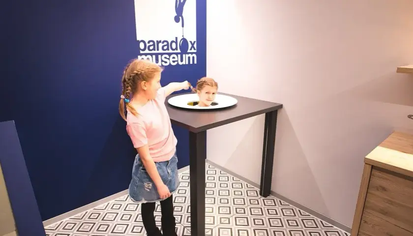 Flicka med flätor pekar på ett huvud som sticker upp ur ett bord på Paradox Museum.