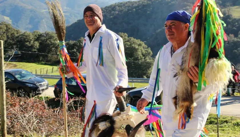 Hombres con trajes blancos y cintas de colores, portando una escoba y una cabeza de cabra, celebran tradiciones de Cantabria.