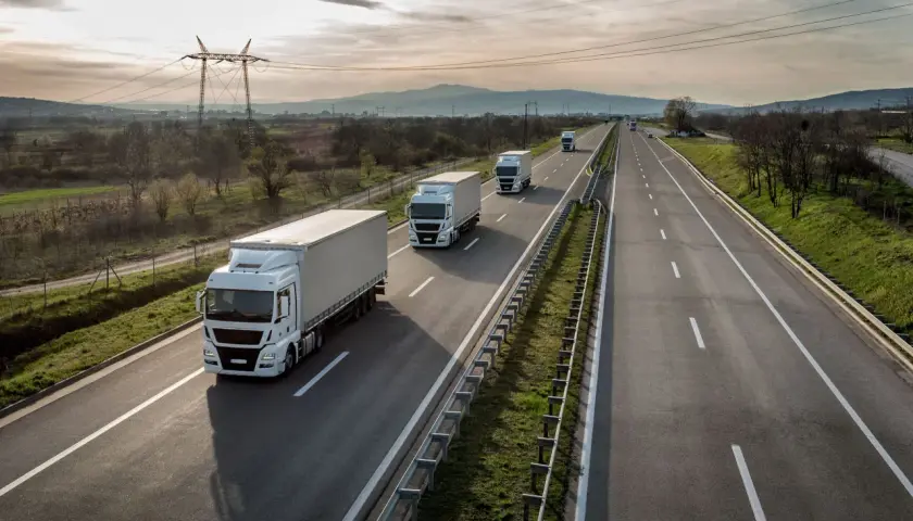 Ciężarówki jadące autostradą, zjazd na bazę pakiet mobilności. W tle góry i linie energetyczne.