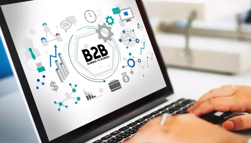 Grafika na ekranie laptopa przedstawia schemat B2B, symbolizujący współpracę biznesową, z ikonami sieci, wykresów i komunikacji.