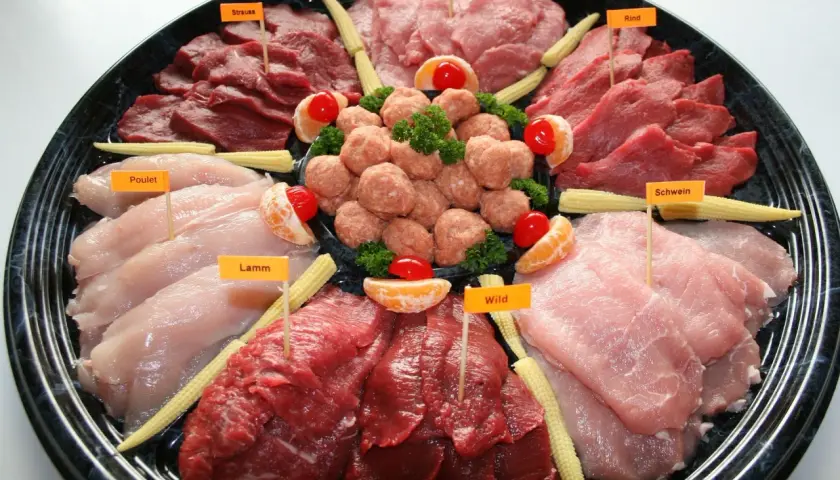 Plateau de viandes variées pour fondue : poulet, agneau, bœuf, porc, veau et gibier, décoré de mini-maïs et d'agrumes.