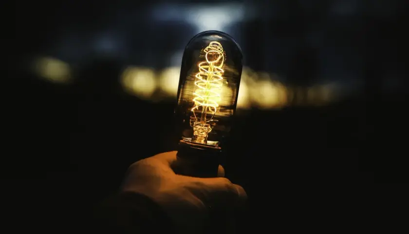 Dłoń trzyma żarzącą się żarówkę Edisona. Zastanawiasz się, ile to wat, gdy świeci 806 lumenów?
