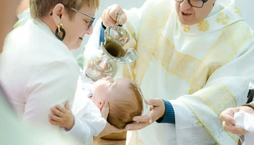 Chrzest dziecka. Kapłan polewa główkę niemowlęcia wodą święconą. Warto wiedzieć, ile kosztuje chrzest, by odpowiednio się przygotować.