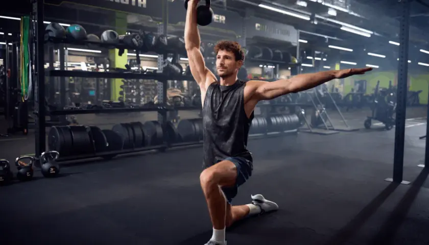 Mężczyzna wykonuje ćwiczenie z kettlebell w siłowni. To część jego zajęć tbc.