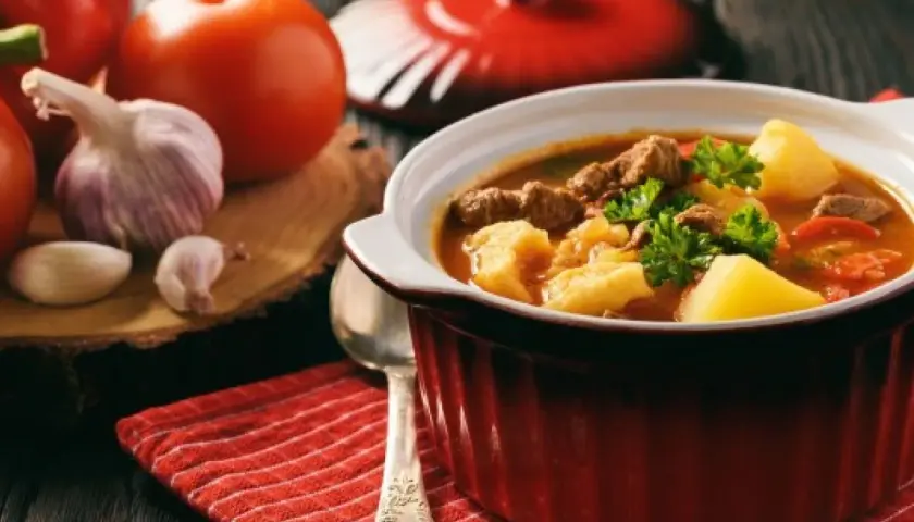 Gorący bogracz z wołowiną i ziemniakami, ozdobiony natką pietruszki, na tle pomidorów i czosnku.