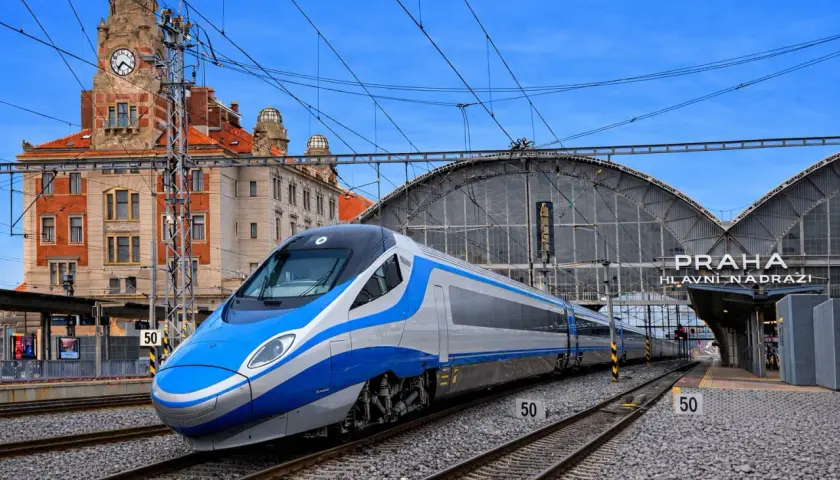 Nowoczesne oznaczenie Pendolino na tle zabytkowego dworca w Pradze. Pociąg w kolorach niebieskim i srebrnym stoi na torach.