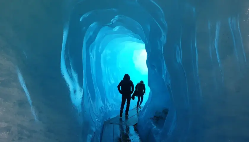 Dwie sylwetki wędrują przez lodowy tunel. Jasne, turkusowe światło przebija się z głębi, tworząc magiczną atmosferę. To jak podróż do wnętrza lodowca, gdzie czas się zatrzymał, a jedynym dźwiękiem jest echo kroków.