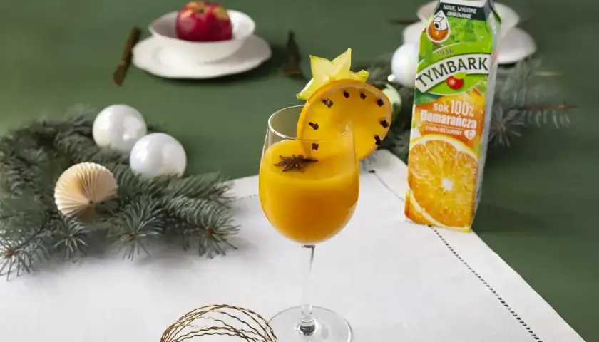 Aromatyczny likier pomarańczowy z goździkami i anyżem, ozdobiony plasterkiem pomarańczy i gwiazdką. Obok karton soku pomarańczowego.