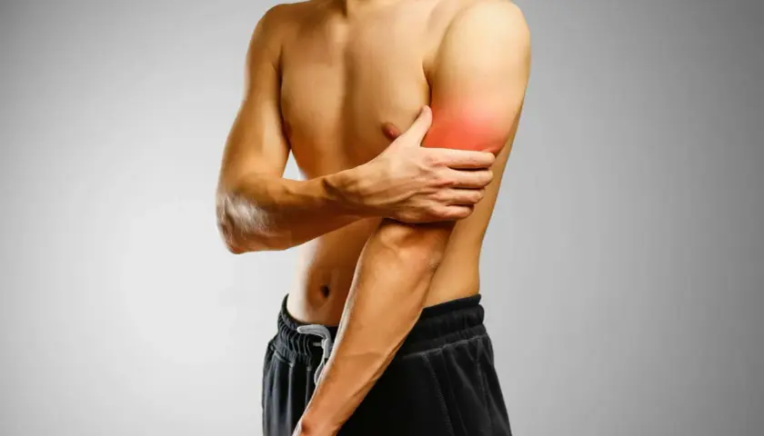 Mężczyzna trzymający się za ramię z zaznaczonym bólem w bicepsie.