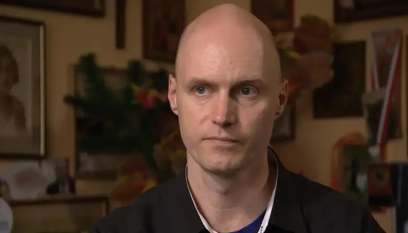 Krzysztof Igor Krawczyk, łysy mężczyzna z niebieskimi oczami, w czarnej koszuli, na tle rodzinnych zdjęć.