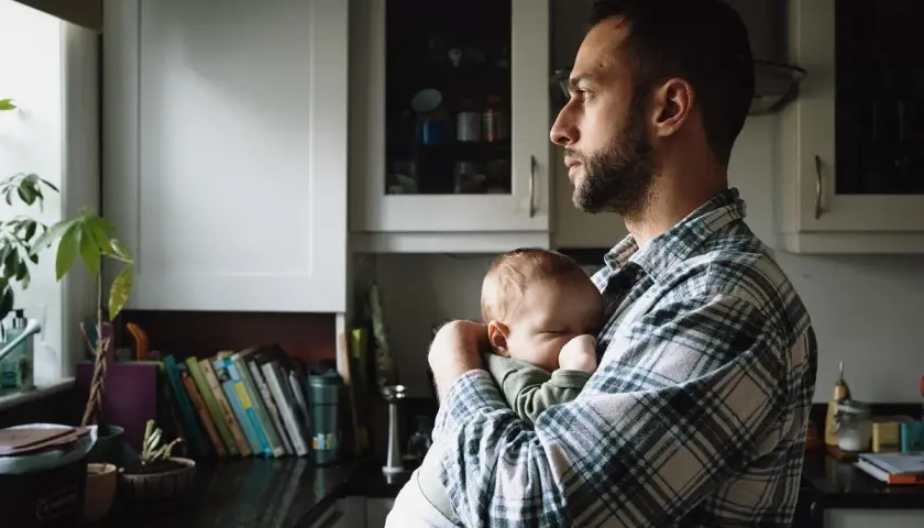 Tata po francusku, czyli "papa", czule tuli swoje śpiące dziecko w kuchni.