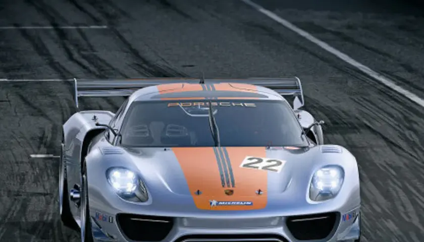 Srebrny Porsche 918 Spyder z pomarańczowymi pasami i numerem 22 na masce pędzi po torze wyścigowym.