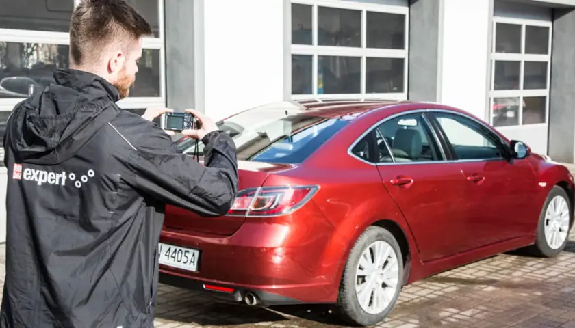 Mężczyzna robi zdjęcie czerwonego samochodu, który jest na sprzedaż bezpośrednio od właściciela.