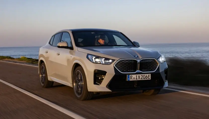 Beżowe BMW iX2 jedzie wzdłuż wybrzeża.