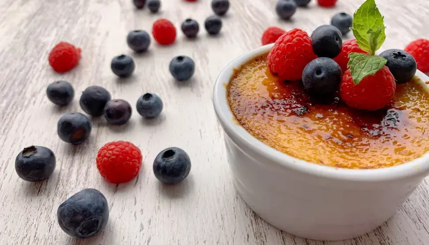 Creme brulee rezept: Ein cremiges Dessert mit karamellisierter Zuckerkruste, garniert mit frischen Beeren und Minze.