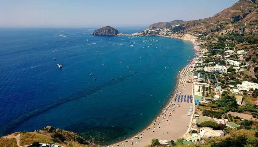 Vista aerea delle spiagge di Ischia, con ombrelloni colorati, mare blu intenso e tante barche all'orizzonte.
