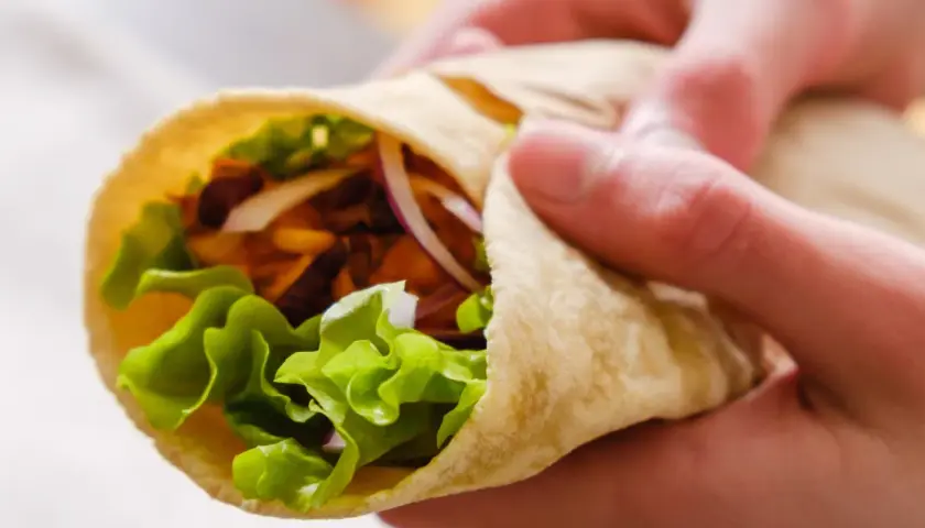 Ręce trzymają świeżą tortillę z sałatą, cebulą i mięsem. Zastanawiasz się, ile kalorii ma tortilla?