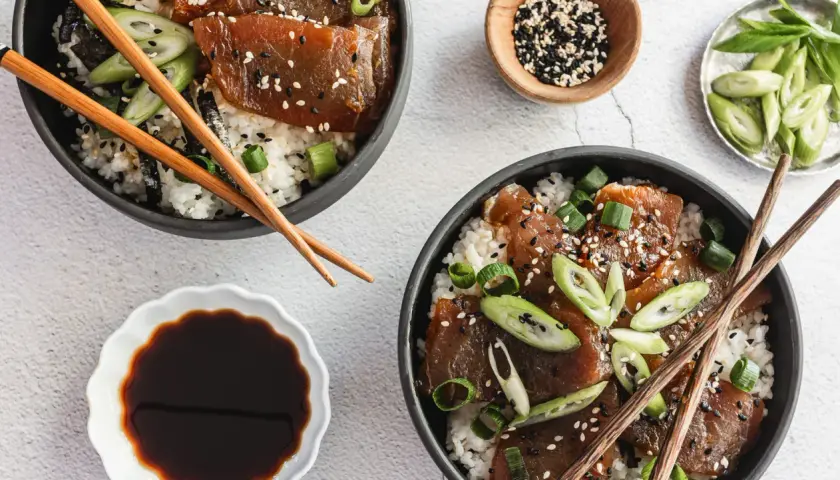 Two bowls of delicious tuna rice don, garnished with sesame seeds and green onions, are ready to be enjoyed with chopsticks.