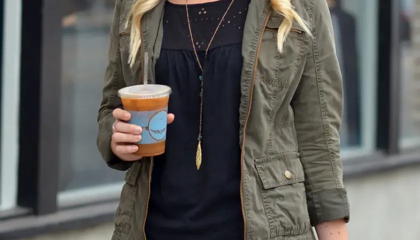 Chica con chaqueta verde militar y café helado.