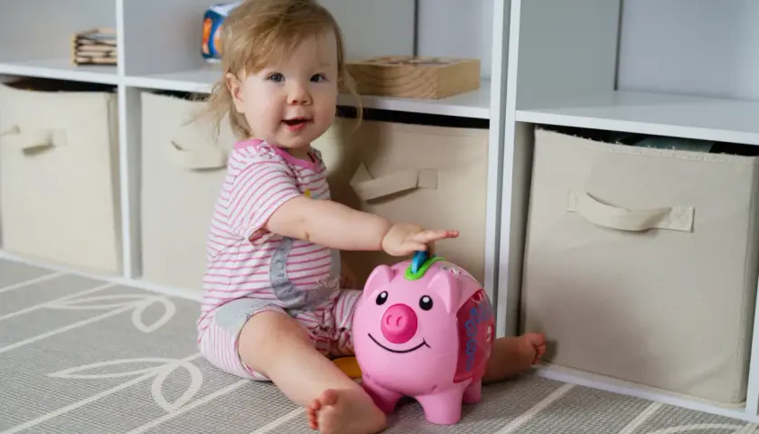 Uśmiechnięta dziewczynka bawi się skarbonką-świnką. To dla niej będzie pierwsze becikowe, gdy nauczy się oszczędzać.