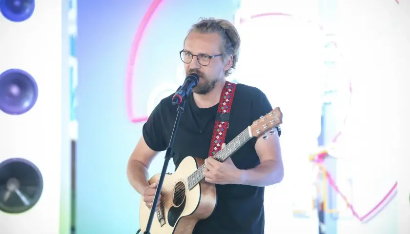 Mężczyzna w okularach gra na gitarze i śpiewa do mikrofonu. Chciałbyś, żeby ktoś powiedział mu "weź się przytul".