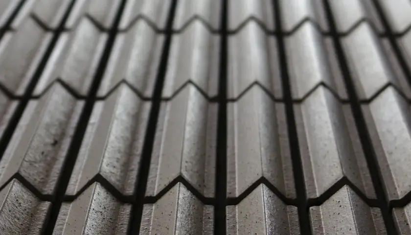 Dettaglio di tegole in cemento, un elemento essenziale per il comfort abitativo, con un pattern a onde che crea giochi di luce e ombra.