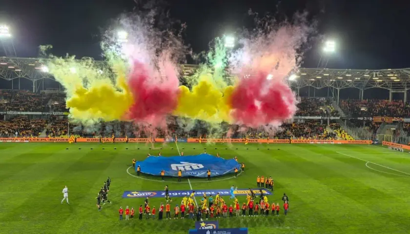 Oprawa meczu Korona Kielce – Jagiellonia Białystok. Piłkarze wychodzą na murawę w otoczeniu gęstego dymu w barwach żółto-czerwonych.