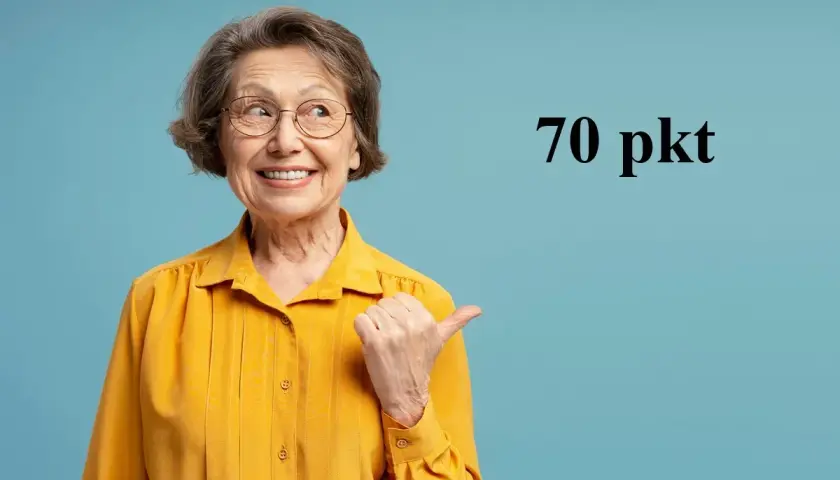 Uśmiechnięta starsza kobieta w okularach i żółtej bluzce wskazuje kciukiem na napis "70 pkt".