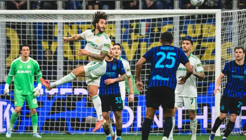 Piłkarz w białej koszulce Inter Mediolan wyskakuje do strzału głową, podczas gdy zawodnik AS Roma z numerem 25 próbuje go zatrzymać.