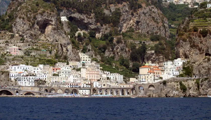 Atrani beach club nestled below dramatic cliffs, with colorful buildings cascading down to the sea.