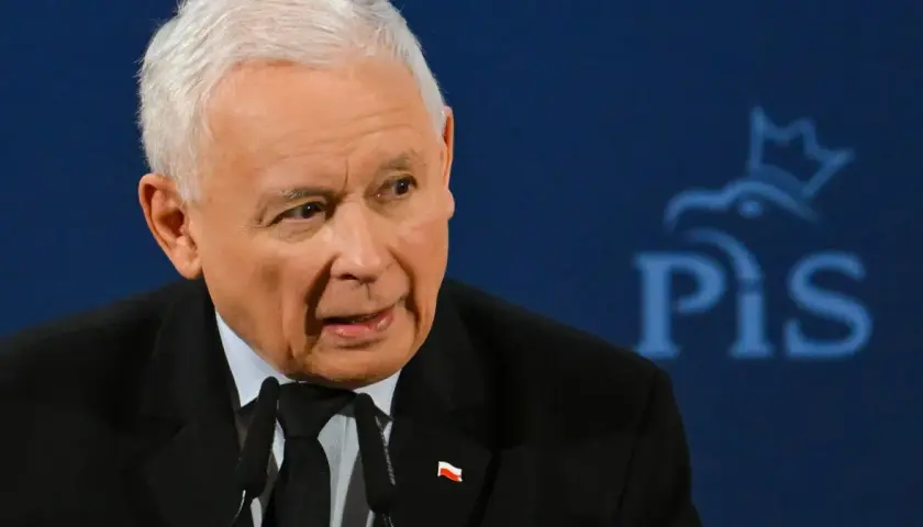Jarosław Kaczyński, w garniturze z polską flagą, przemawia na tle logo PiS. Czy Jarosław Kaczyński faktycznie planuje oddać władzę młodszym politykom?