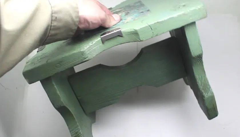 Mano che tiene uno sgabello di legno verde, pronto per verniciare con bomboletta spray.