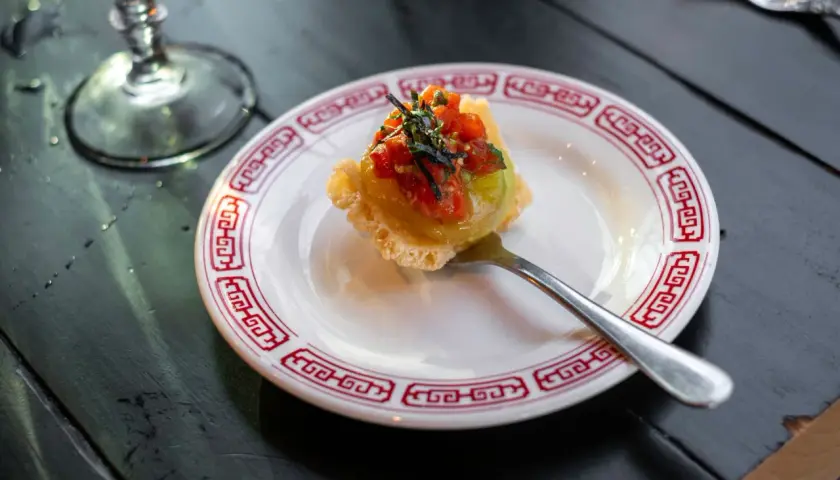 Wykwintny amuse bouche z awokado i pomidorkami na chrupiącym spodzie, podany na talerzyku z czerwonym wzorem.