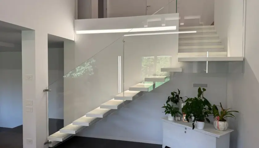 Moderna scala a sbalzo con parapetto in vetro, illuminazione integrata e un'elegante balaustra. Perfetta per il vano scale di una villa moderna.