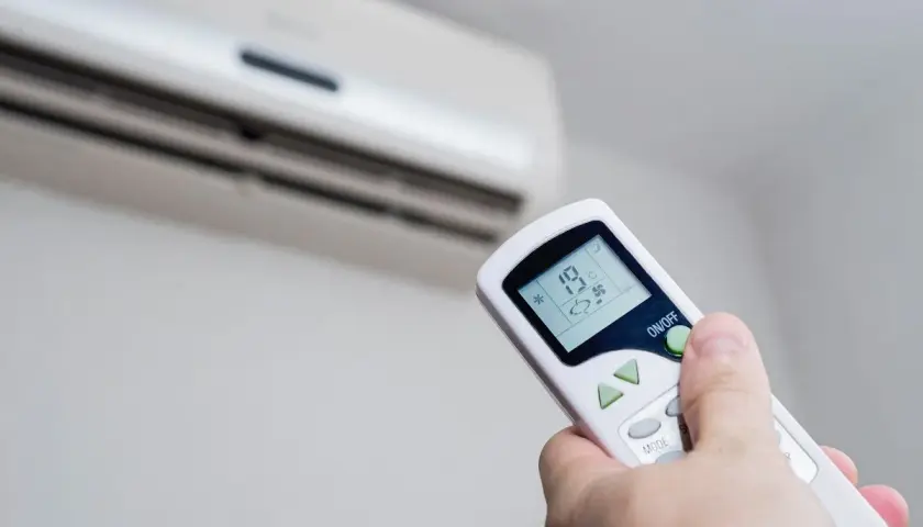 Mando a distancia ajustando la temperatura ideal aire acondicionado para ahorrar energía. Se ve el aire acondicionado y la mano con el control.