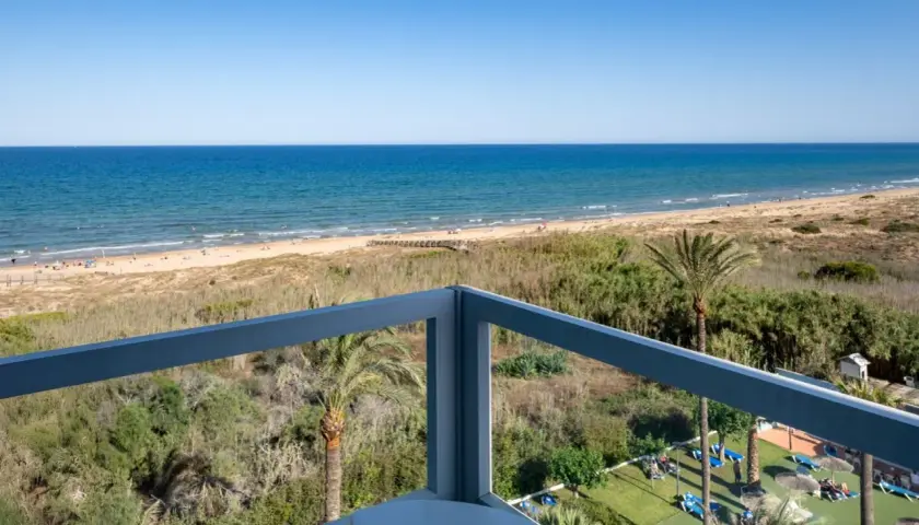 Vista desde balcón de hotel, mar azul, playa con gente y vegetación. Opiniones de hotel Playas de Guardamar positivas.