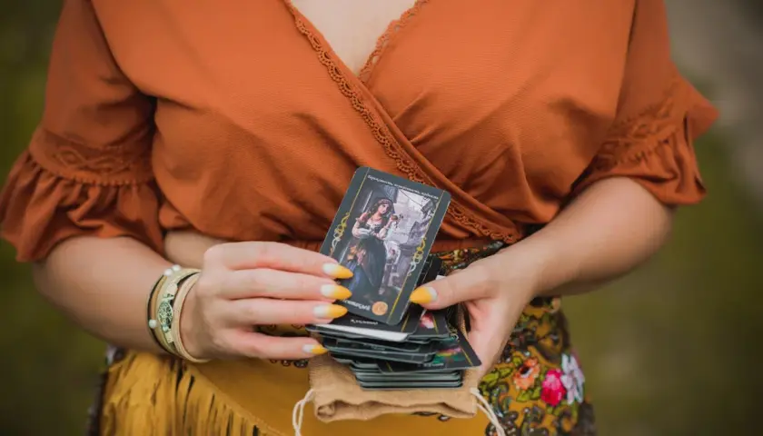 Kobieta trzyma talię kart, jedną z nich jest koło fortuny tarot.