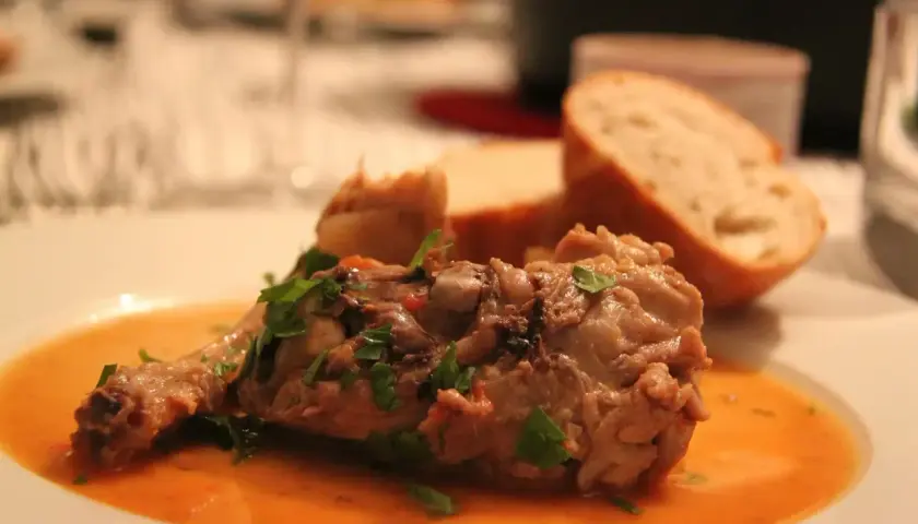 Un plat savoureux de viande mijotée, garni de persil frais, servi avec du pain. Parfait pour accompagner un osso bucco.