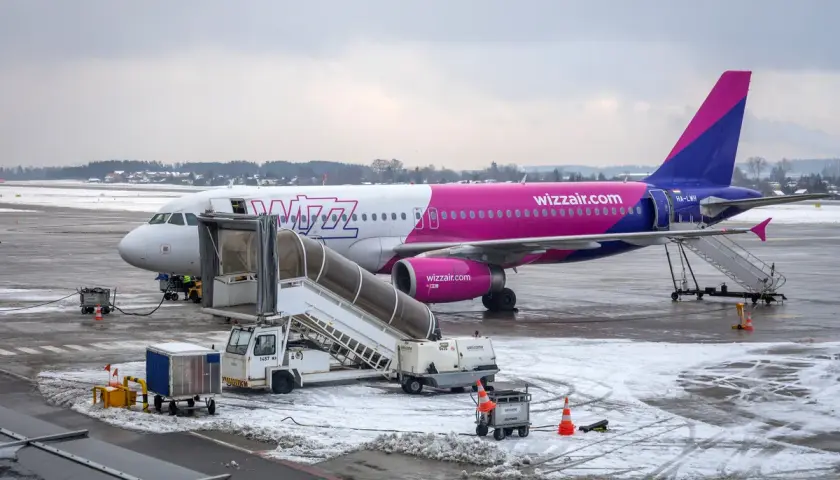 Samolot Wizz Air na lotnisku zimą, z drabiną i sprzętem naziemnym.