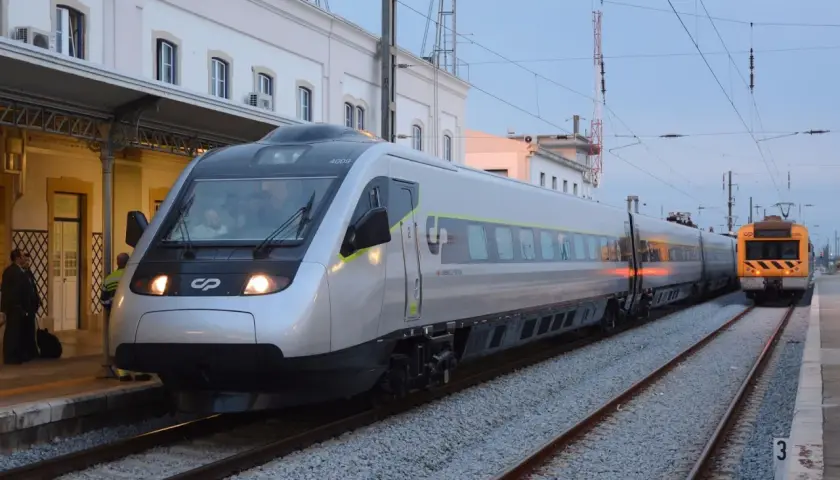 Tren moderno plateado y otro amarillo en estación, listos para el viaje de Lisboa a Oporto.
