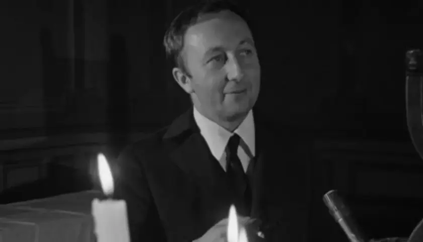 Bogumił Kobiela w jednym z filmów, w eleganckim garniturze, przy blasku świec.