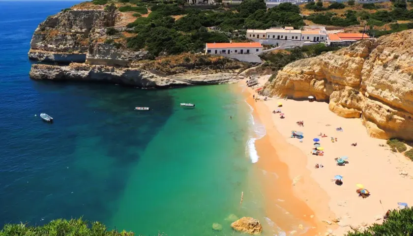 Playa dorada con aguas turquesas y acantilados, ideal para tu plan de algarve en 6 dias. Casas blancas coronan la colina.