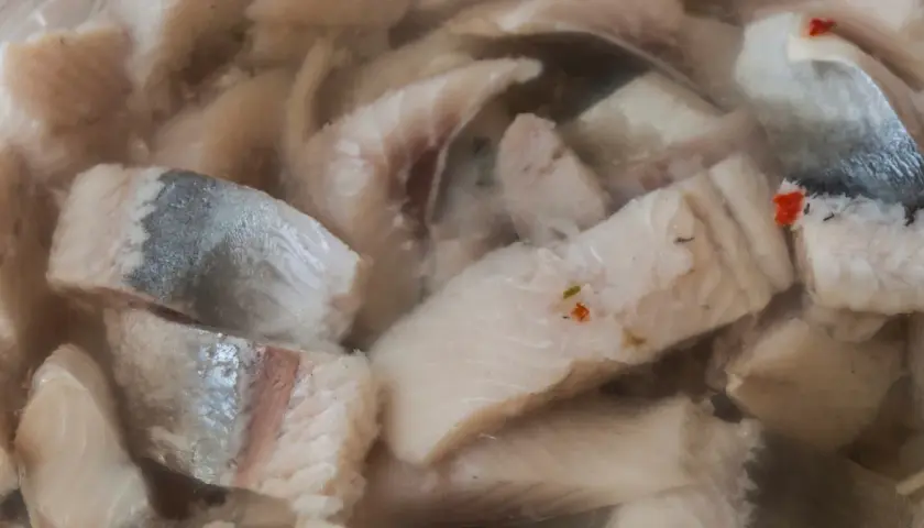 Kawałki kiszonych śledzi w zalewie, niektóre z drobinkami przypraw.