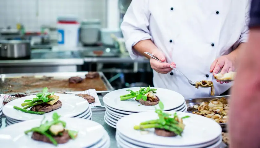 Ein Koch garniert Steaks mit Spargel und Pilzen. Das Gehalt eines Kochs hängt von Erfahrung und Restaurant ab.