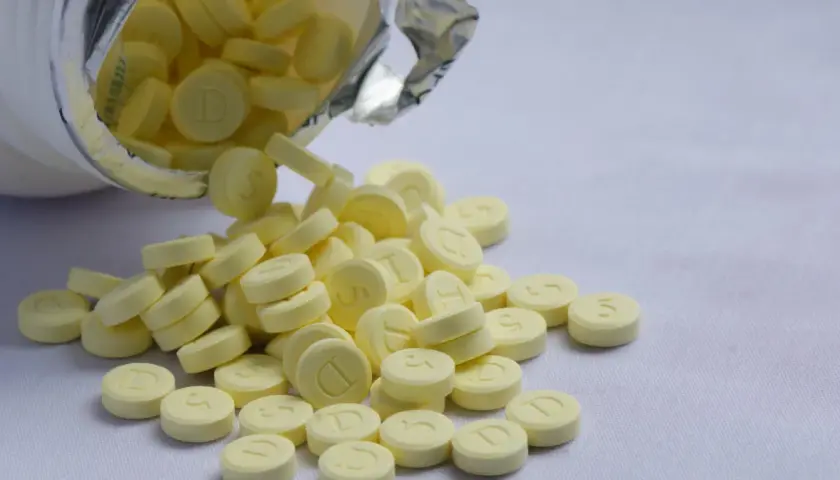 Żółte tabletki, niektóre z literą "D", inne z cyfrą "5", wysypują się z białego opakowania. To może być relanium.