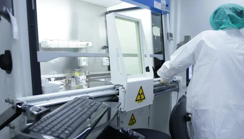 Pracownik w kombinezonie ochronnym pracuje w laboratorium, gdzie widoczne są ostrzeżenia o promieniowaniu radioaktywnym.