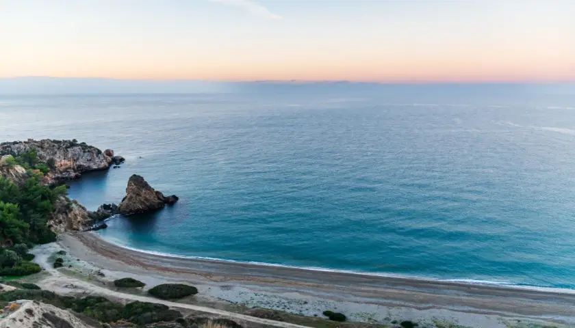 Vista aérea de una cala rocosa y una playa de guijarros en las playas de Málaga al amanecer.